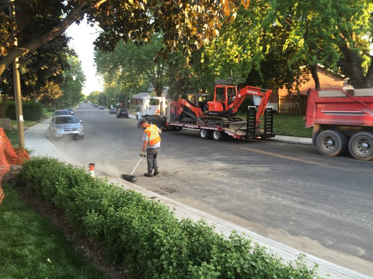 Ouvrier qui nettoie la rue suite a des travaux de remplacement de drain français avec un balai mécanique.