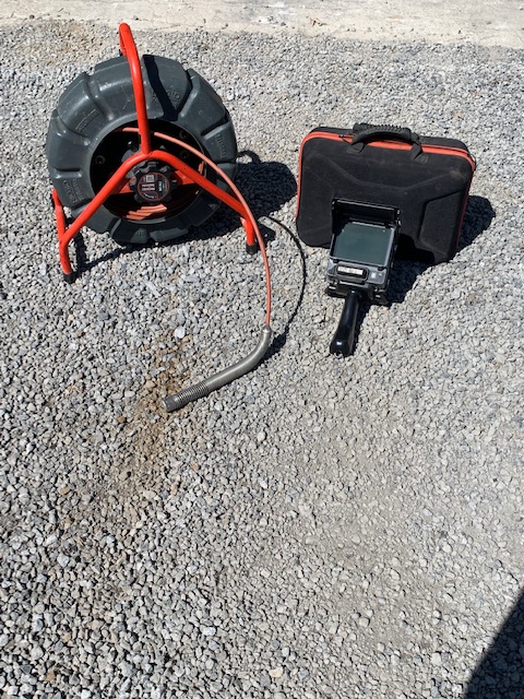 Caméra numérique d'inspection de conduite d'égout et de drain français avec son moniteur déposés sur le sol.