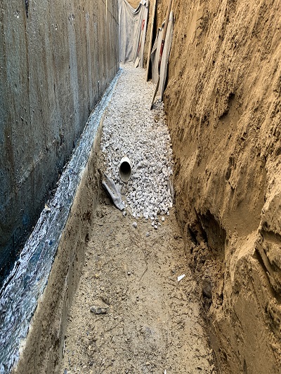 Tuyau de drain français dans le fond de la tranchée d'excavation enrobé de pierre.