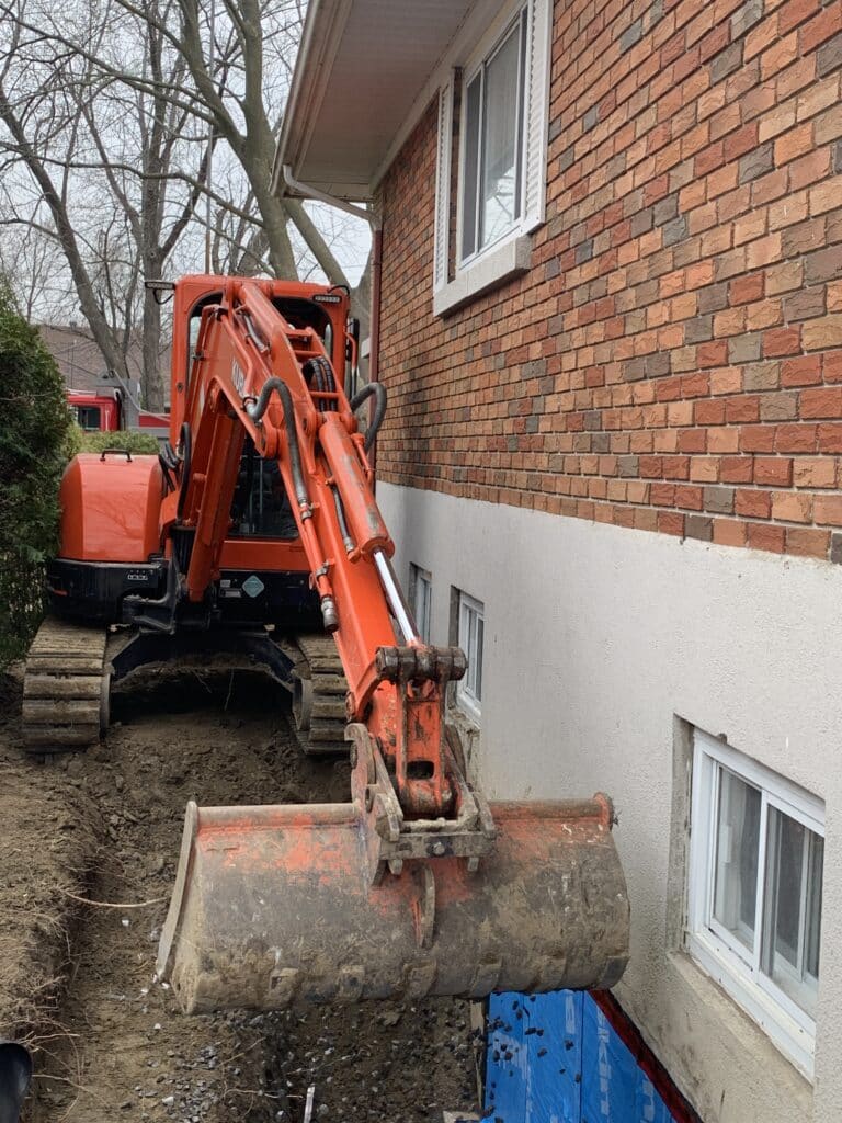 mini-excavatrice effectuant le remblais d'une fondation suite a des travaux d'installation de drain français.